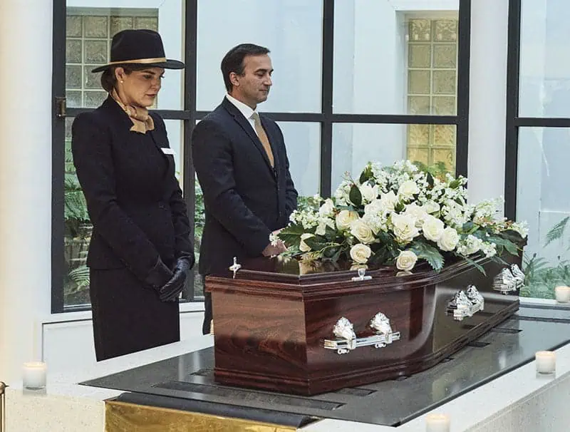 Two funeral directors at a perth cremation service next to a coffin with funeral flowers